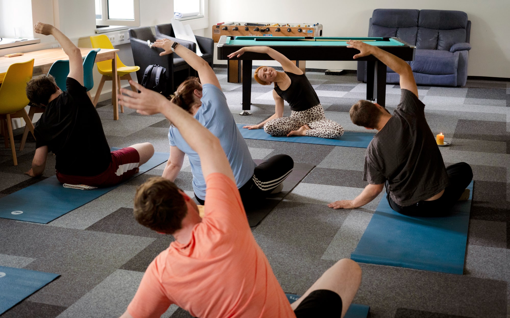 Mitarbeiter:innen von TRICERA energy machen Yoga-Übungen mit einer Lehrerin. Dahinter ein Billiard-Tisch und Kicker.